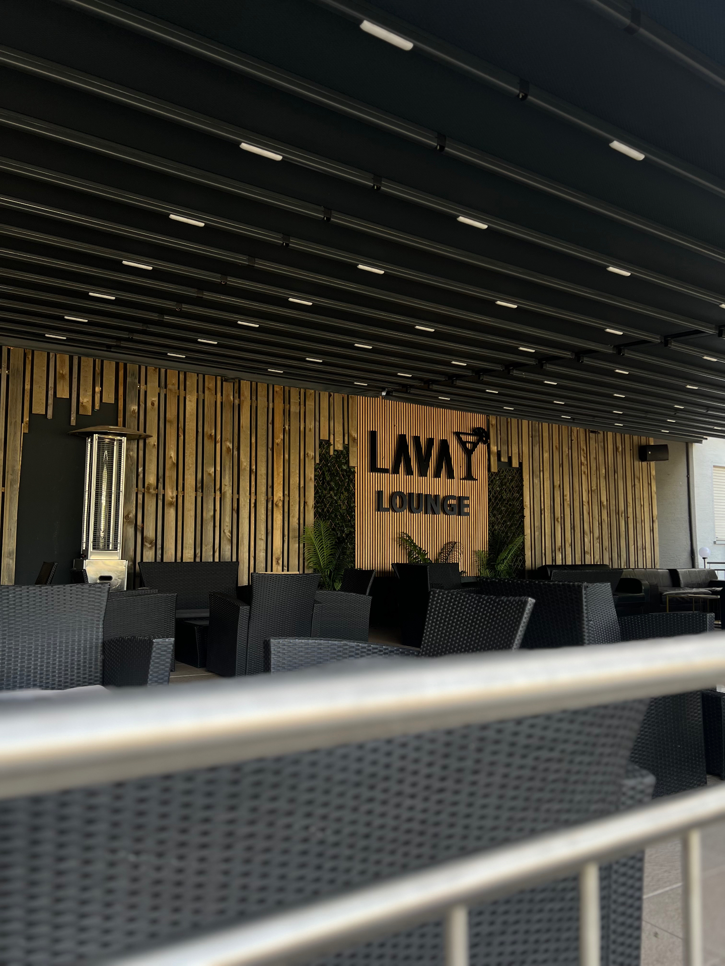 Überdachte Terrasse mit Lava Lounge Schriftzug an der Holzlamellenwand